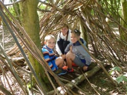 three children in a shelter made from sticks in a wood